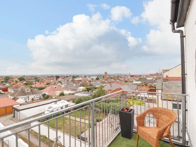 A balcony with a wicker chair a tall planter and a view of rooftops and houses at Ty Uchaf in Rhyl