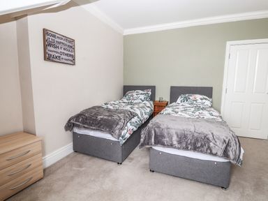 A bedroom with two single beds with floral bedding and grey throws with wooden nightstand between the beds a wooden chest of drawers on the side and a motivational sign on the wall at Ty Uchaf in Rhyl