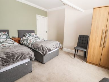 A bedroom with two single beds a wooden wardrobe and a black chair at Ty Uchaf in Rhyl