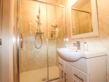 A bathroom with a shower enclosure and a white sink cabinet with a mirror above at Ty Uchaf Rhyl