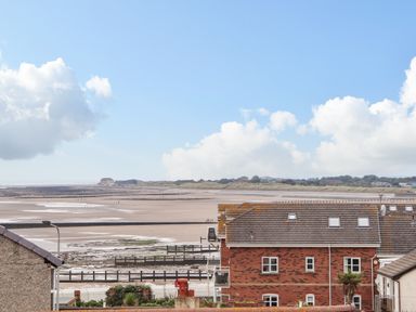 A beach with sand and water viewed from behind houses at Ty Uchaf in Rhyl
