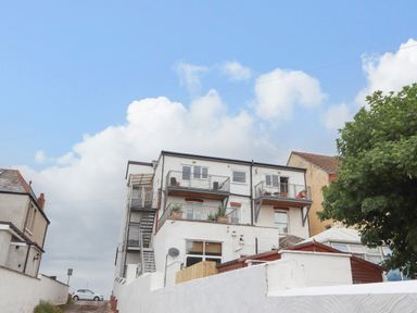 A multi-story white residential building with balconies and external staircases in Rhyl