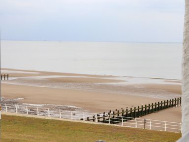 A sandy beach with a wooden groyne and a railing along a grassy area at Ty Uchaf in Rhyl