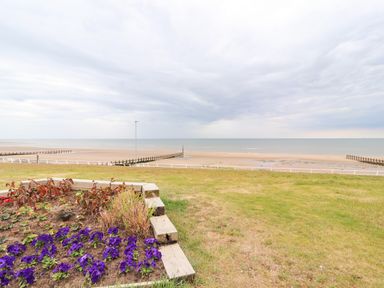 A flower bed with purple flowers and grass overlooking a sandy beach and sea at Ty Uchaf in Rhyl
