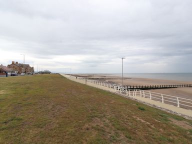 A coastal promenade with a grassy area a walkway railings and a sandy beach at Ty Uchaf in Rhyl