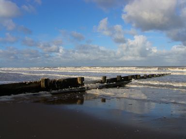 A beach with waves and a wooden groyne extending into the sea at Ty Uchaf in Rhyl