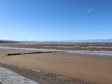A sandy beach with a wooden groyne and waves under a clear blue sky at Ty Uchaf in Rhyl