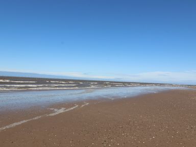 A sandy beach with waves and a clear blue sky at Ty Uchaf in Rhyl