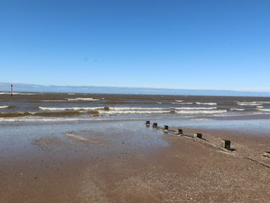 A sandy beach with wooden groynes and waves under a blue sky at Ty Uchaf in Rhyl