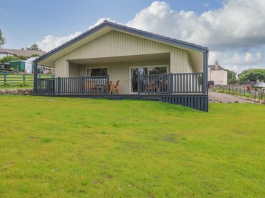 A house with a porch and wooden furniture overlooking a grassy lawn at The Lodge in Blairgowrie