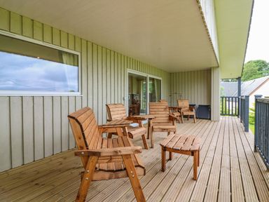 A covered wooden deck with wooden chairs and tables outside a house at The Lodge in Blairgowrie