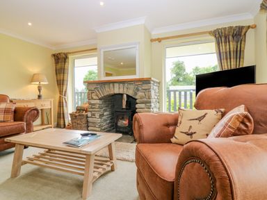 A living room with leather armchairs a wooden coffee table a stone fireplace and two windows at The Lodge in Blairgowrie