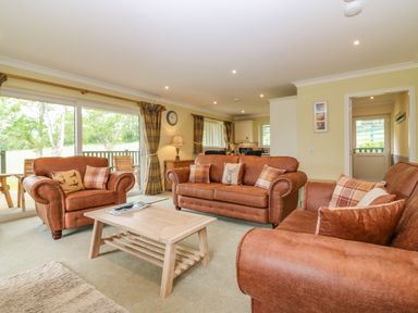 A living room with three brown sofas a wooden coffee table sliding glass doors and a lamp at The Lodge in Blairgowrie