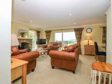 A living room with brown sofas a stone fireplace a television and a desk with a chair at The Lodge in Blairgowrie