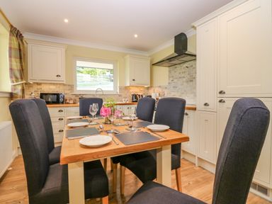 A kitchen with a dining table set for six with black chairs and white cabinets at The Lodge in Blairgowrie