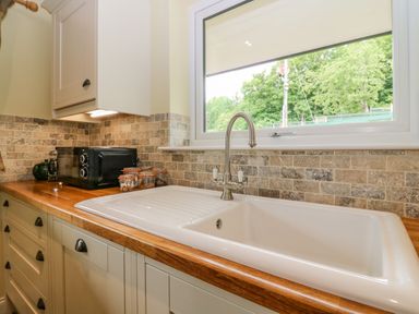A kitchen countertop with a white sink a silver faucet a black microwave and glass jars under a window with trees outside at The Lodge in Blairgowrie