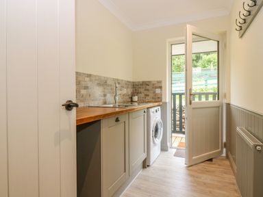 A utility room with a sink countertop washing machine and door leading outside at The Lodge in Blairgowrie