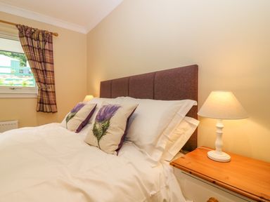 A bedroom with a bed with floral pillows bedside lamps and a window with plaid curtains at The Lodge in Blairgowrie