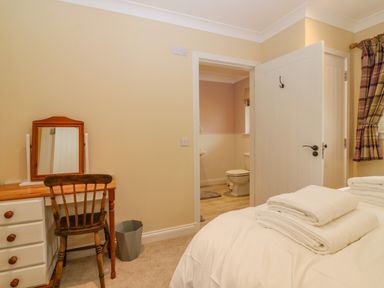 A bedroom with a wooden chair and desk with mirror and white towels on bed at The Lodge in Blairgowrie