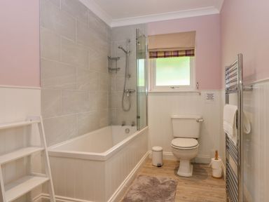 A bathroom with a bathtub shower combination a toilet a window with a blind a towel rack and a small shelving unit at The Lodge in Blairgowrie