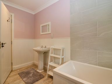 A bathroom with a bathtub sink mirror small shelf and door at The Lodge in Blairgowrie