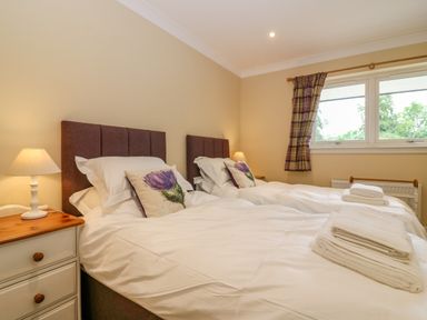 A bedroom with two single beds, bedside tables with lamps, windows with curtains and folded towels on beds at The Lodge in Blairgowrie