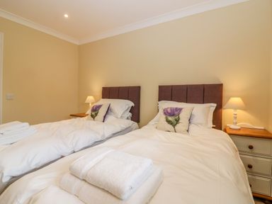 A bedroom with two single beds white bedding bedside tables with lamps and decorative pillows at The Lodge in Blairgowrie