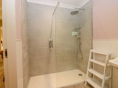 A walk in shower with glass partition and shelves next to a white sink at The Lodge in Blairgowrie