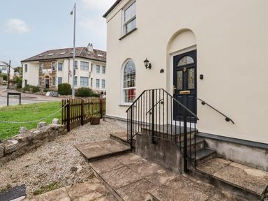 The entrance of a building with stone steps and a black door next to a window and a grassy area at 2 Old Talbot Cottages in Lostwithiel