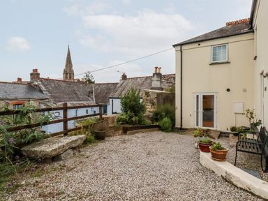 An outdoor gravel courtyard with potted plants a bench stone seating and old buildings in the background at 2 Old Talbot Cottages in Lostwithiel