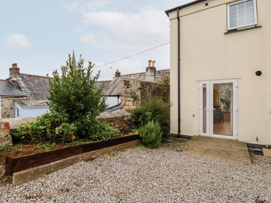 A gravel outdoor area with plants and a white building with glass doors at 2 Old Talbot Cottages in Lostwithiel