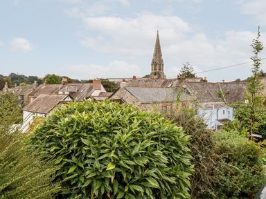 A view of rooftops with a church steeple and greenery in the foreground at 2 Old Talbot Cottages in Lostwithiel