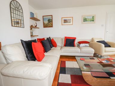 A living room with white sofas and black and red cushions a glass coffee table and paintings on the wall at 2 Old Talbot Cottages in Lostwithiel