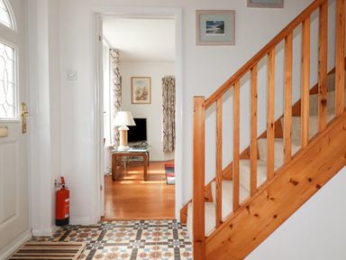 An entryway with patterned tile flooring a wooden staircase and a view into a living room with a TV and lamp at 2 Old Talbot Cottages in Lostwithiel