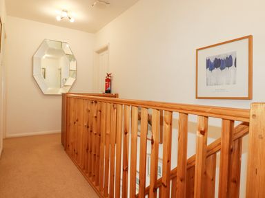 A hallway with wooden stair railing a mirror fire extinguisher and framed artwork at 2 Old Talbot Cottages in Lostwithiel