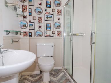 A bathroom with a toilet sink shower and wallpaper with framed pictures at 2 Old Talbot Cottages in Lostwithiel