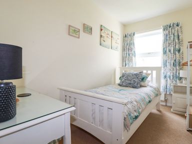 A small bedroom with a single bed with pillows and a quilt a desk with a lamp and paintings on the wall at 2 Old Talbot Cottages in Lostwithiel