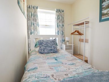 A small bedroom with a single bed a bedside table with a lamp an open wardrobe with hangers and a window with patterned curtains at 2 Old Talbot Cottages Lostwithiel