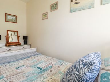 A bedroom with a bed, a dresser with a mirror and lamps, and framed pictures on the wall at 2 Old Talbot Cottages in Lostwithiel