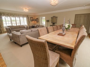 A dining area with a wooden table and upholstered chairs next to a seating area with sofas and armchairs in a large room at Bodmin Country House in Lanivet