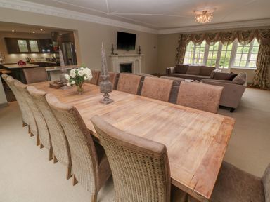 A dining room with a long wooden table and chairs next to a living area with sofas and a fireplace at Bodmin Country House in Lanivet