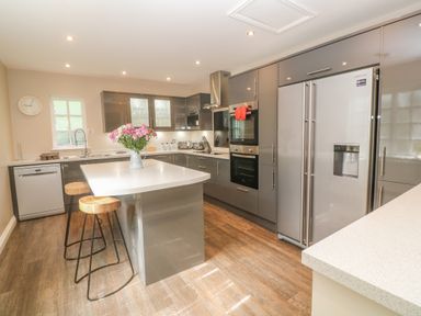 A kitchen with grey cabinets a kitchen island with stools and flowers on the island at Bodmin Country House in Lanivet