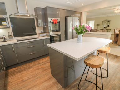 A kitchen with gray cabinets an island with flowers on top and wooden stools at Bodmin Country House in Lanivet