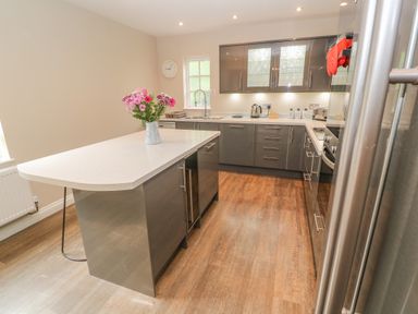 A kitchen with an island countertop with flowers in a vase and cabinets at Bodmin Country House in Lanivet