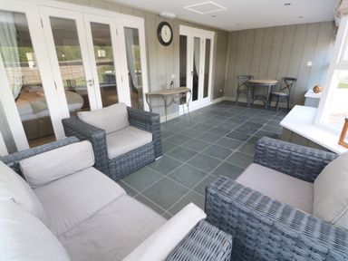 A sunroom with wicker furniture including chairs and a sofa a small table with two chairs and glass doors leading to another room at Bodmin Country House in Lanivet