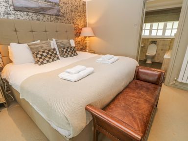 A bedroom with a bed with towels on it a leather bench and an open door to a bathroom at Bodmin Country House in Lanivet