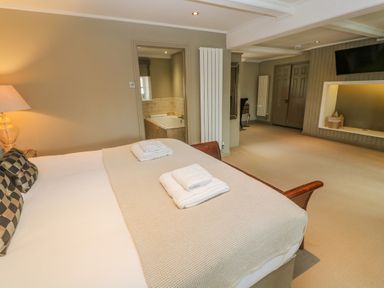 A bedroom with a bed facing a TV and an open door showing a bathroom with a bathtub at Bodmin Country House in Lanivet