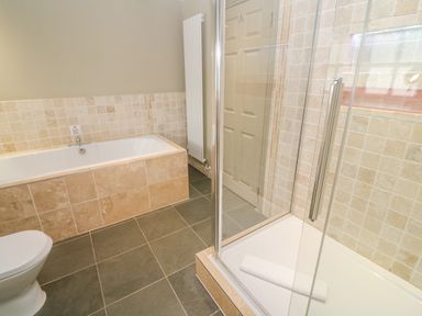 A bathroom with a bathtub, glass-enclosed shower, white toilet, and tiled walls at Bodmin Country House in Lanivet