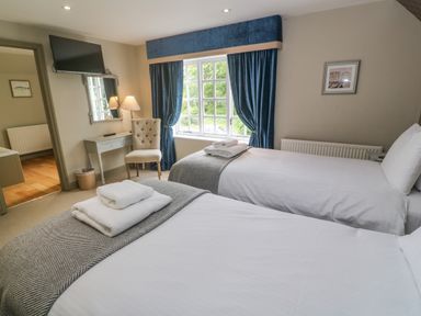 A bedroom with two single beds a chair and a desk below a wall mounted TV at Bodmin Country House in Lanivet