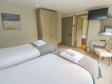 A bedroom with two single beds towels on beds wardrobe doors and a wall mounted television at Bodmin Country House in Lanivet